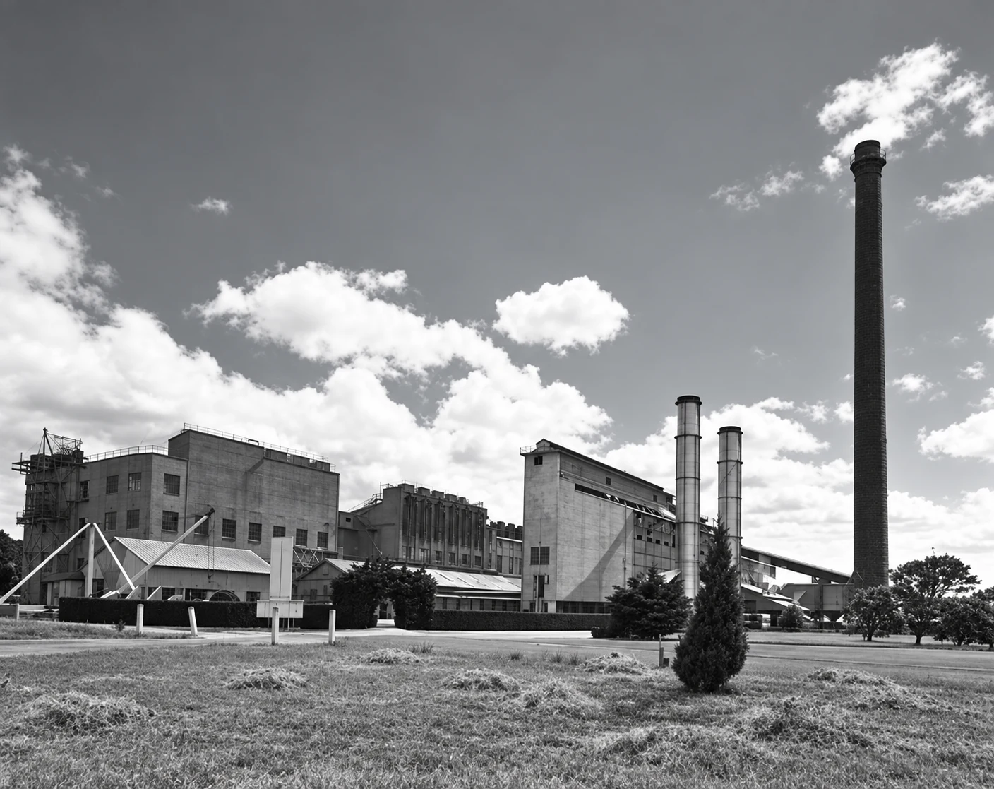 Black-and-white exterior view of the Yallourn briquette works, with several factory buildings and four tall chimneys beneath a bright sky.