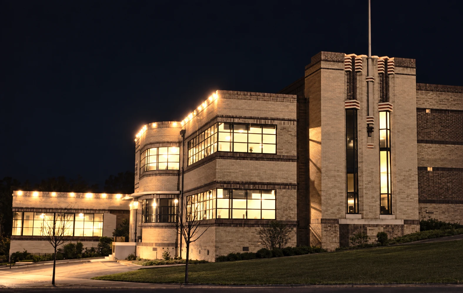 Restored night-time colour view of the Yallourn technical education building, with light glowing through its long windows.