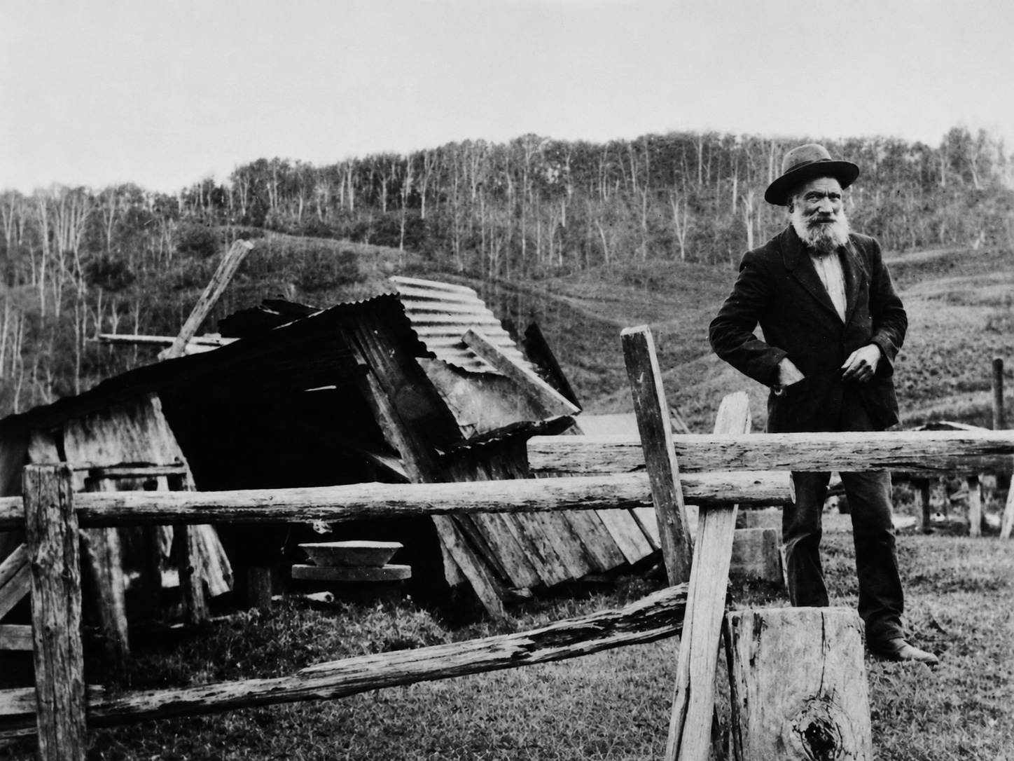 Restored black-and-white photograph of Andy Anderson standing beside a timber and corrugated-iron hut on the Yallourn North hillside.