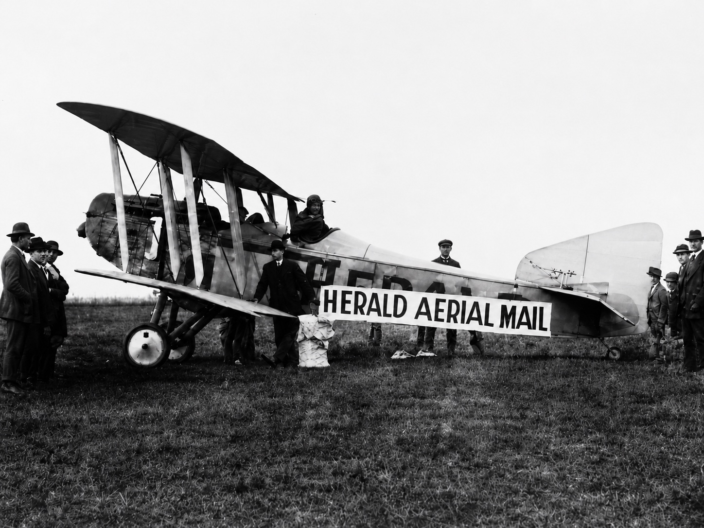 Restored black-and-white photograph of a biplane carrying a Herald Aerial Mail banner, surrounded by people before its 1920 Gippsland delivery flight.