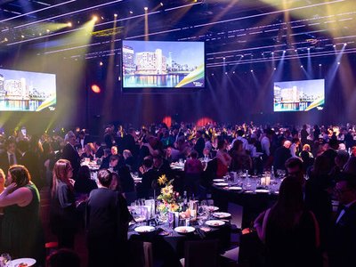 A conference audience of tourism professionals seated in a large performing arts centre, with a speaker on stage and event branding visible.
