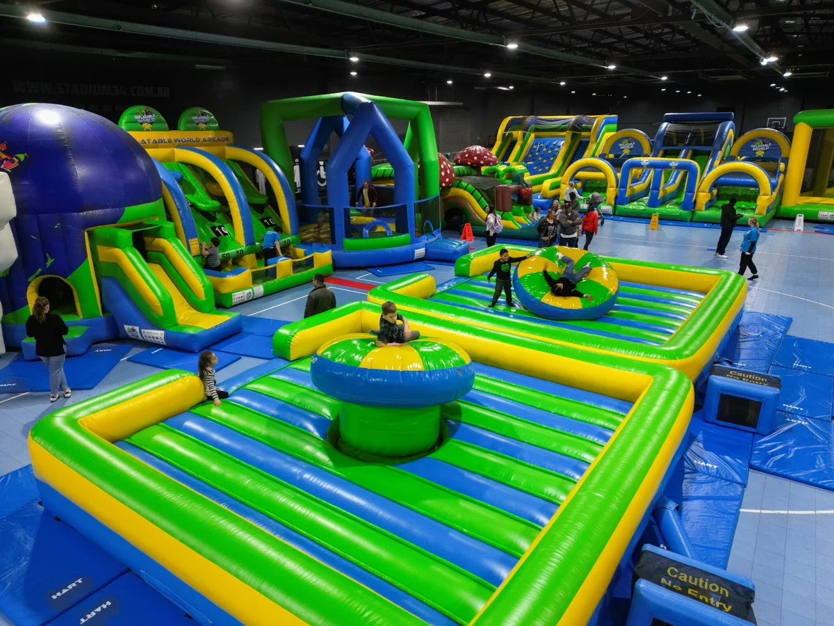 A wide view across the colourful Inflatable World playground inside Stadium 34, with families moving among slides and obstacle courses.