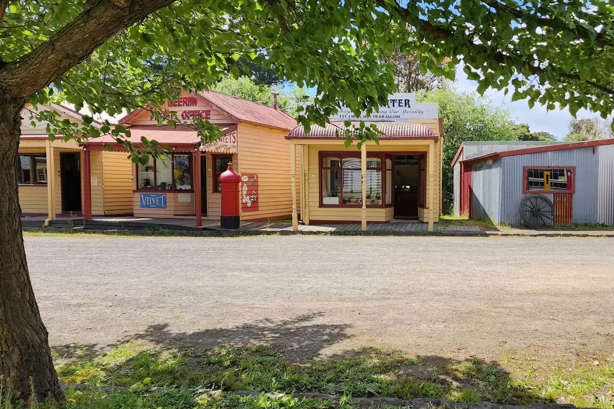 Old Gippstown's main street, with timber shopfronts and a corrugated-iron building beneath a leafy tree.