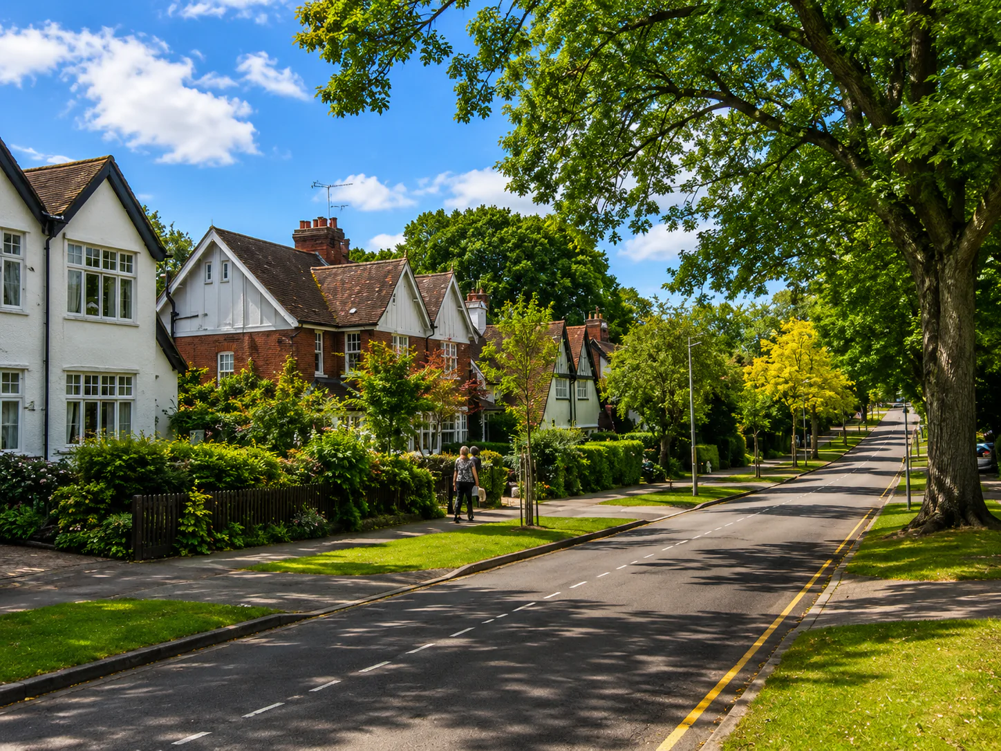 Tree-lined residential street with large gardens and white and brick houses.