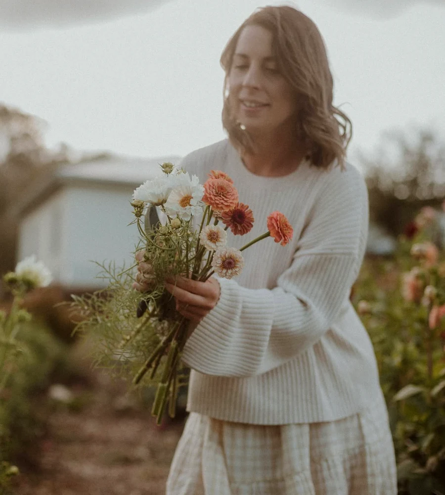A woman holding freshly cut pink and white flowers among garden beds.