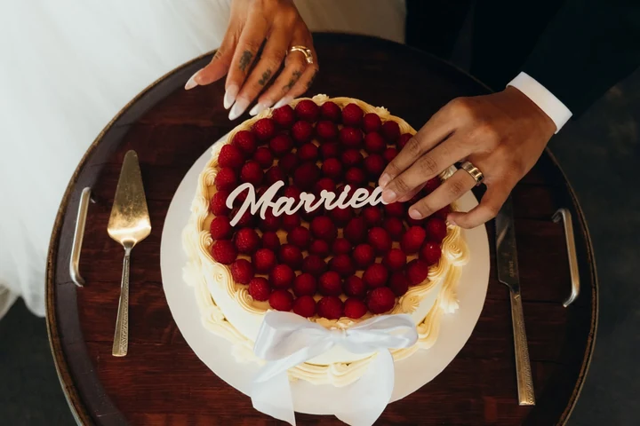 Hands place a white Married cake topper onto a raspberry-covered wedding cake.