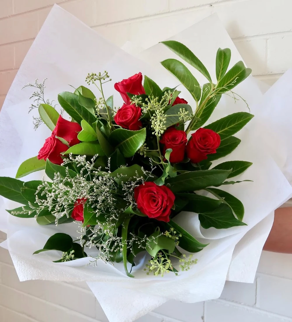 A bouquet of red roses and green foliage wrapped in white paper.