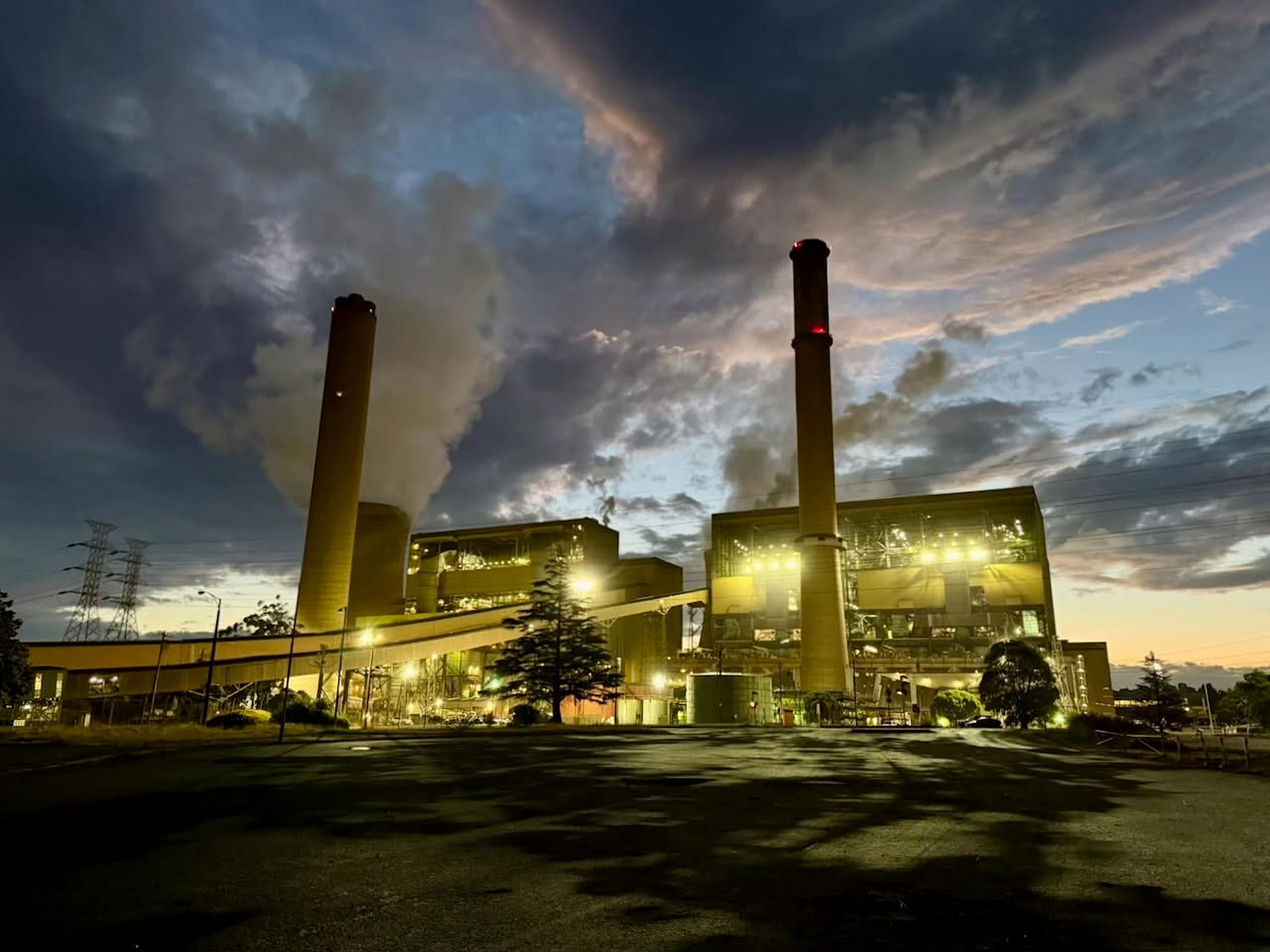 Yallourn Power Station operating beneath a dramatic evening sky, with tall chimneys and illuminated generation buildings.
