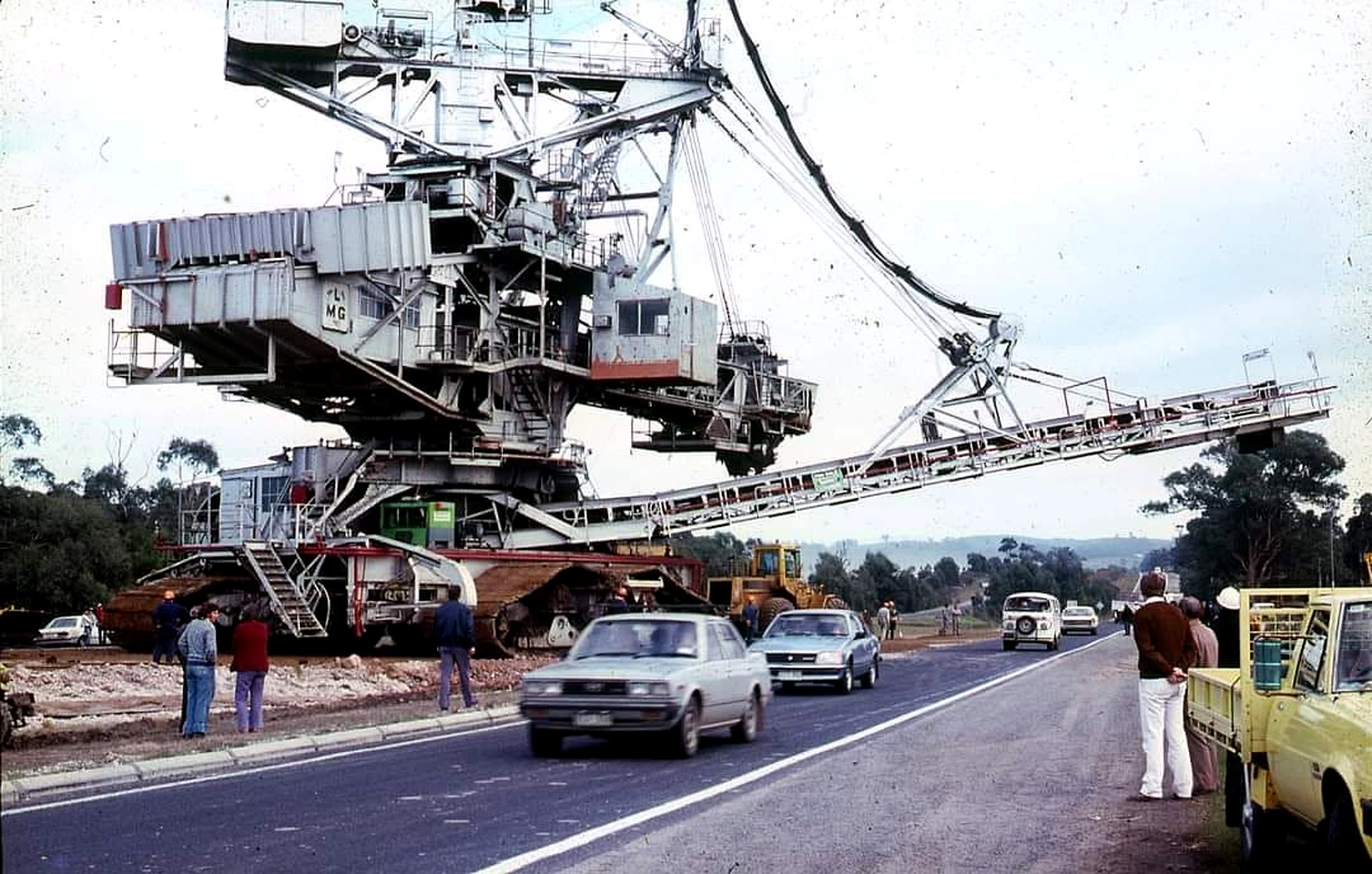Large coal-mining dredger crossing the Princes Highway as cars and onlookers wait.