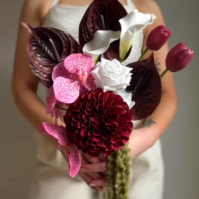 A person holds a sculptural bouquet of deep burgundy, pink and white flowers.