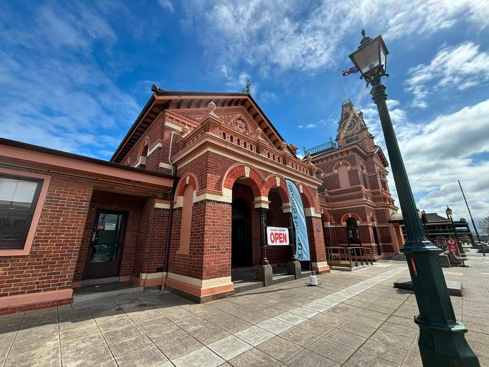 An open sign stands beneath the arches of Traralgon Courthouse, with its clock tower rising behind.