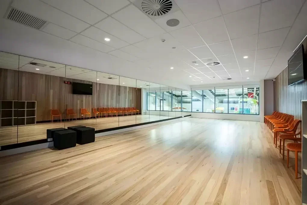 A bright timber-floored activity room has a mirrored wall and orange chairs at Gippsland Regional Aquatic Centre.