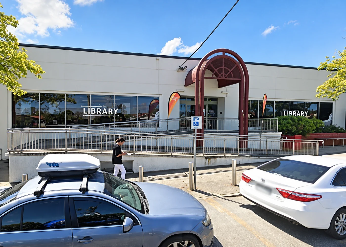 A restored view of Morwell Library's white façade, red arched entrance and access ramp from across the street.